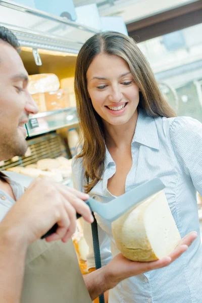 Shop assistant determining with customer where to slice cheese — Stock Photo, Image