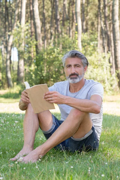 Hombre acostado en la hierba leyendo un libro — Foto de Stock