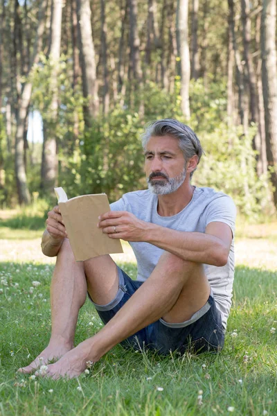 Lyingsitting muž v trávě, čtení knihy — Stock fotografie