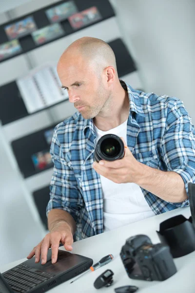 Homem segurando lente da câmera e usando laptop — Fotografia de Stock