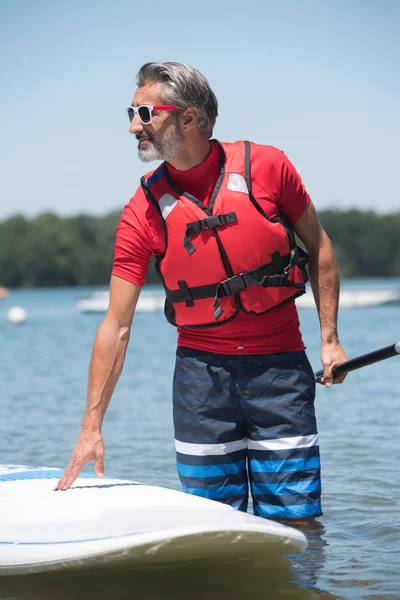 Mannen bredvid en stand-up paddle board på sjön — Stockfoto