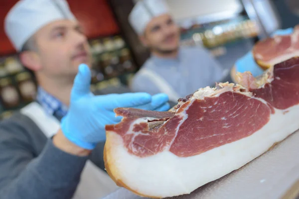 Carniceros mostrando gran pedazo de jamón a los clientes — Foto de Stock