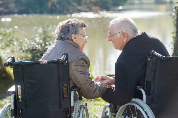 Älteres Ehepaar im Rollstuhl greift zueinander — Stockfoto