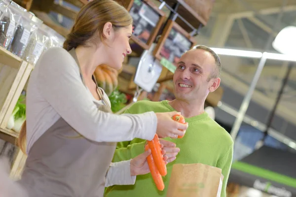 Asistente de tienda pasando zanahorias al cliente —  Fotos de Stock