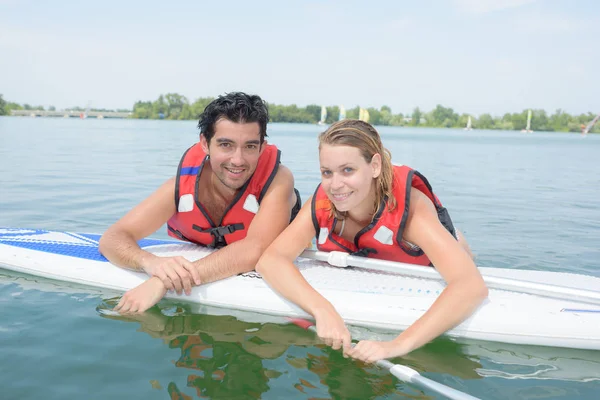 Jong koppel zwemmen met paddle board in een meer — Stockfoto