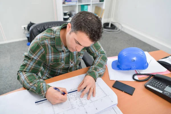 Uomo seduto alla scrivania a lavorare su cianografie — Foto Stock