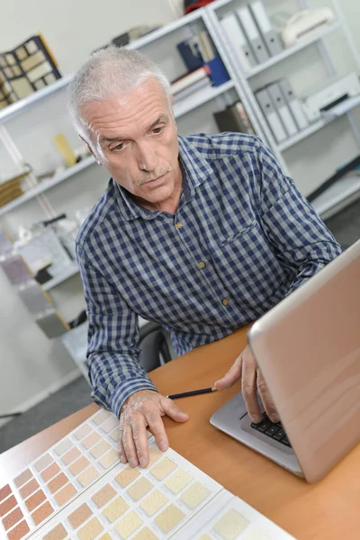 Uomo sul computer portatile, guardando la tabella di vernice — Foto Stock