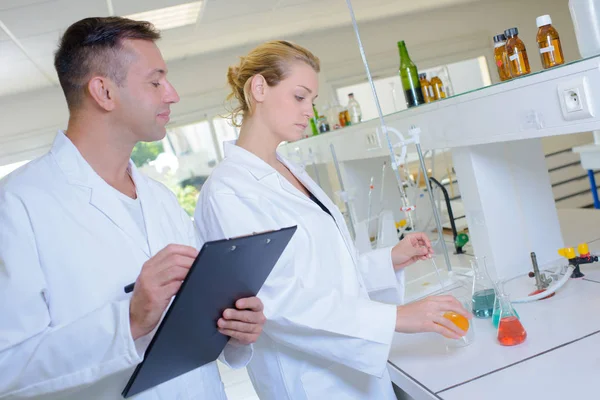 Homem com prancheta assistindo mulher trabalhador de laboratório — Fotografia de Stock