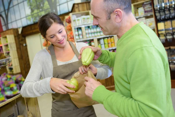 Assistente de loja ajudando o homem a colocar frutas no saco de papel — Fotografia de Stock