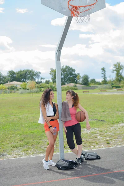 Ladies leaning against post of basketball net — Stock Photo, Image