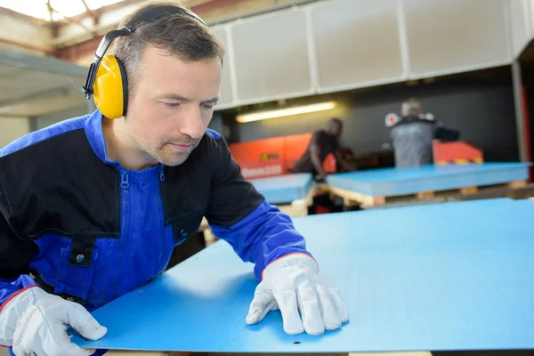 Trabalhador olhando para marca na folha azul de material — Fotografia de Stock