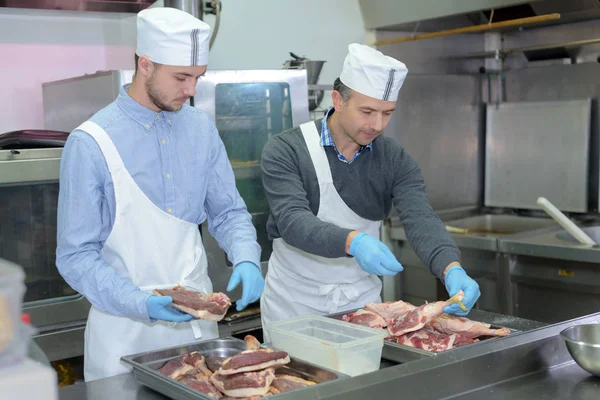 Apprenti et chef préparant la viande dans la cuisine du restaurant — Photo