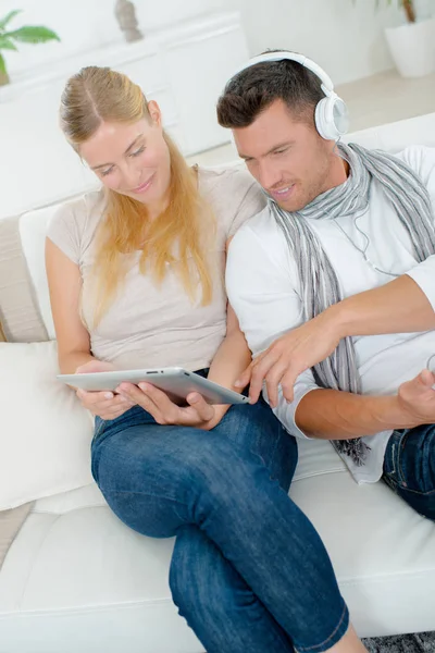 Pareja en casa, mujer en la tableta, hombre usando auriculares —  Fotos de Stock