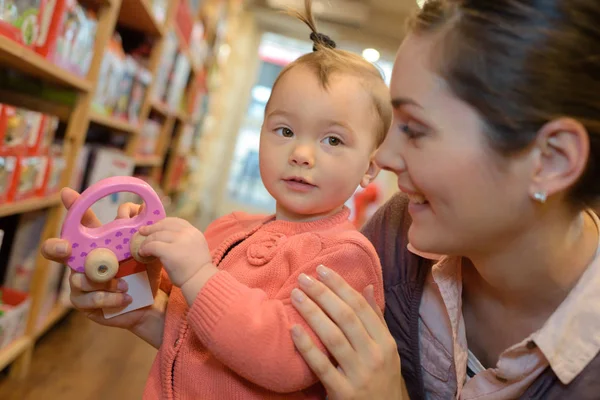 年轻母亲，她的女儿在玩具商店购物 — 图库照片