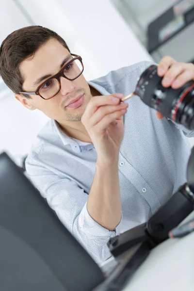 Jovem técnico confiante está consertando e limpando um cameralense digital — Fotografia de Stock