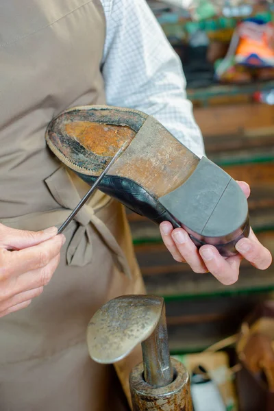 Cobbler scraping sole of shoe with a knife