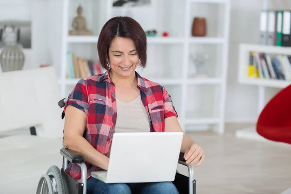 Gehandicapte vrouw op rolstoel met laptop thuis — Stockfoto