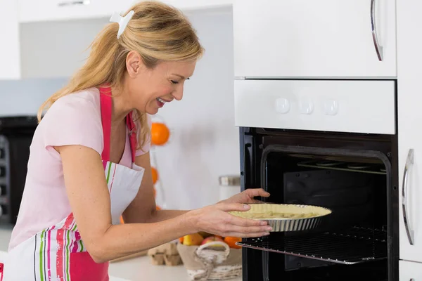 Pretty blond woman putting tart in the oven for baking — Stock Photo, Image