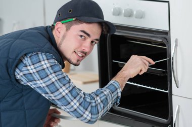 young repairman in overall installing brand new oven in kitchen clipart