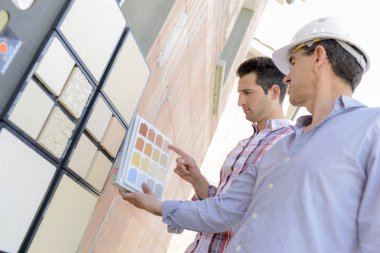 Two men matching colour samples on exterior wall clipart
