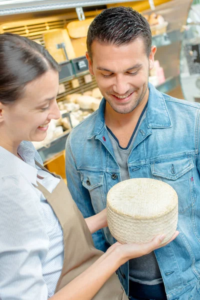 Κατάστημα Βοηθός κρατώντας τυρί, δείχνοντας πελάτη — Φωτογραφία Αρχείου