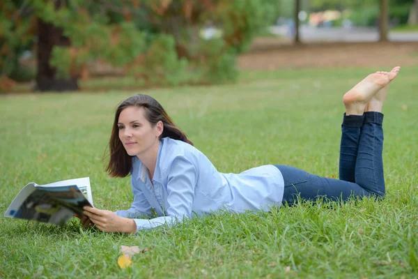Женщина лежала на траве читая журнал — стоковое фото