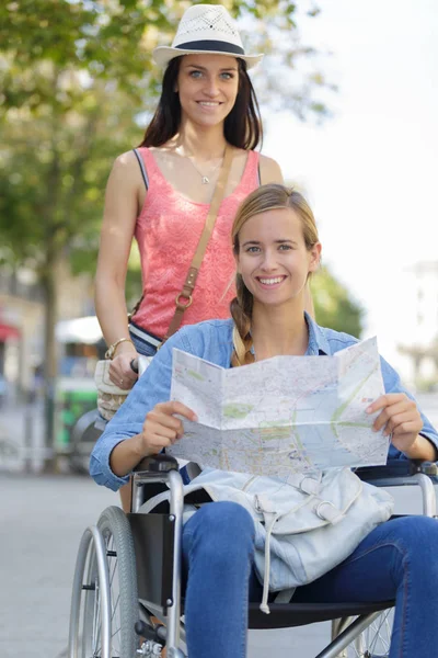 Deux amis visitant la ville étrangère un assis en fauteuil roulant — Photo