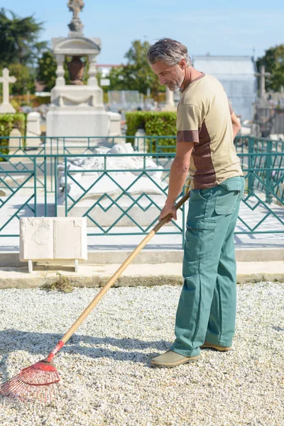 Homme ratissant du gravier dans le cimetière — Photo