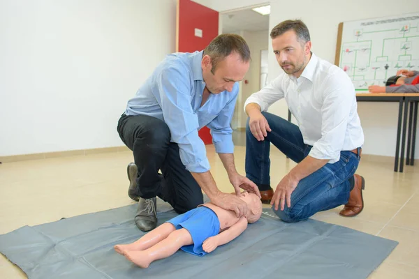 Hombres realizando primeros auxilios en un maniquí de tamaño infantil — Foto de Stock