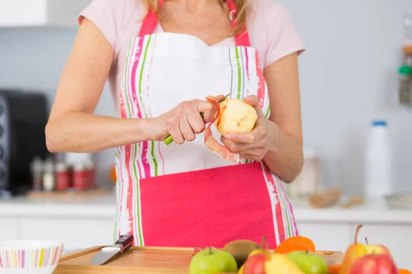 Starsza kobieta obieranie jabłek w kuchni — Zdjęcie stockowe