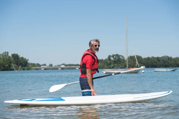 Homem ao lado de um stand-up paddle board no lago — Fotografia de Stock