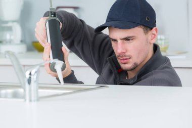 young handyman applying silicone sealant with gun around sink clipart