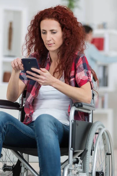 Handikappade rödhårig kvinna skicka SMS och surfa på sin smartphone — Stockfoto