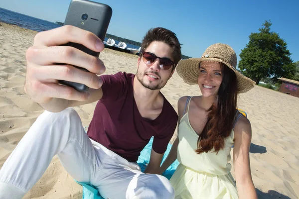 Wspaniała Młoda para siedzi na plaży i robić selfie — Zdjęcie stockowe
