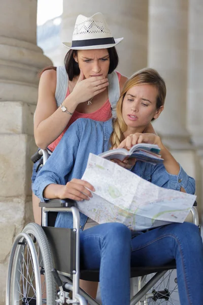 Deux amis visitant la ville étrangère un assis en fauteuil roulant — Photo