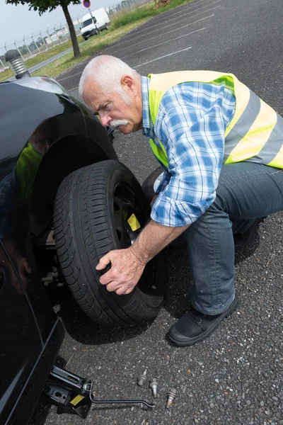 Aged man changing leaking tire on the verge — Stock Photo, Image