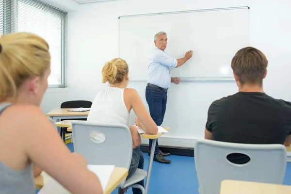 Teacher writing on white board in front of class — Stock Photo, Image