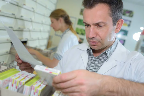 Farmacêutico segurando pacientes prescrição e à procura de medicação — Fotografia de Stock