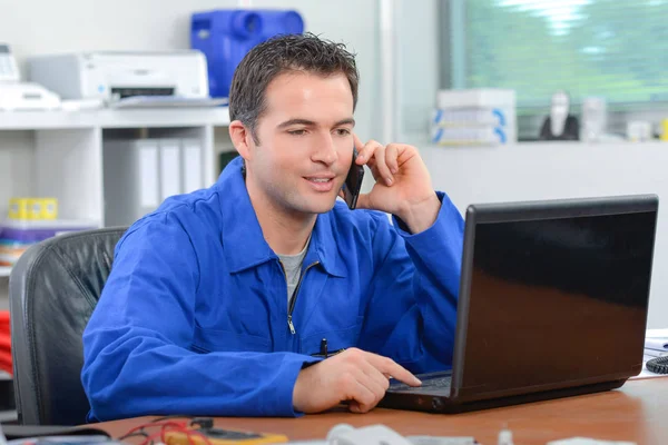 Mannen i overaller på laptop och prata på telefon — Stockfoto