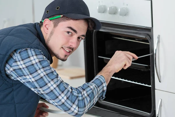 Joven reparador en general la instalación de horno nuevo en la cocina — Foto de Stock