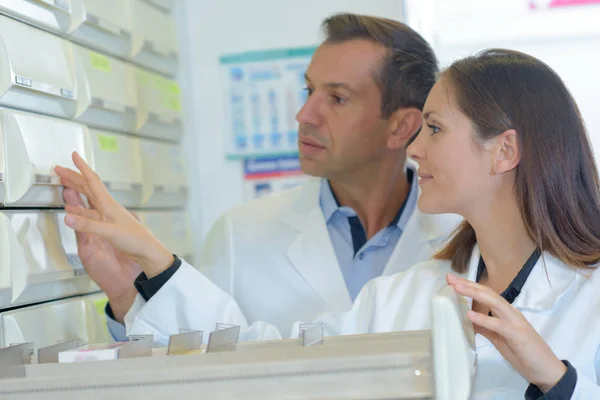 Pharmacists looking at medication in drawer — Stock Photo, Image