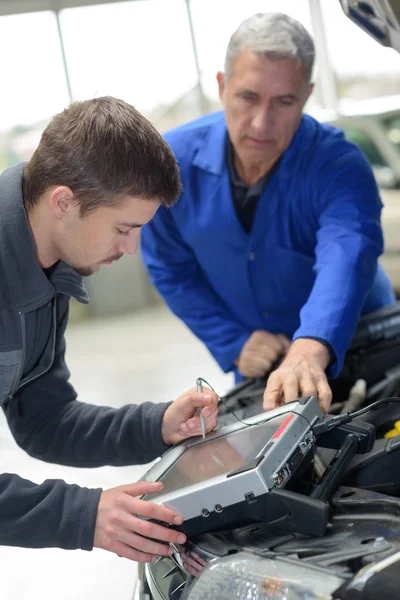 Mecánico y aprendiz trabajando en coche con ordenador — Foto de Stock