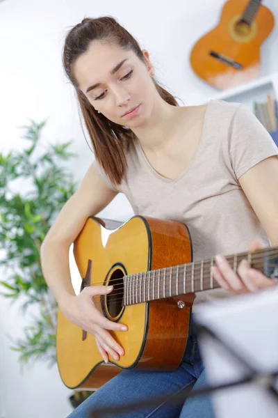 Menina bonita sentada no sofá e tocando guitarra — Fotografia de Stock