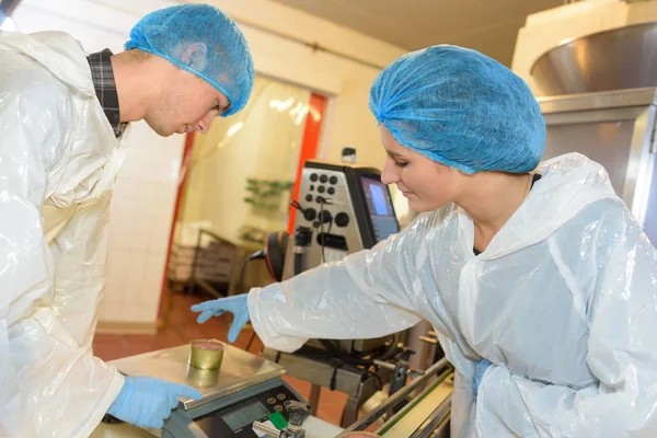 Fabriksarbetare väger metall tin av föda på skalor i fabrik — Stockfoto