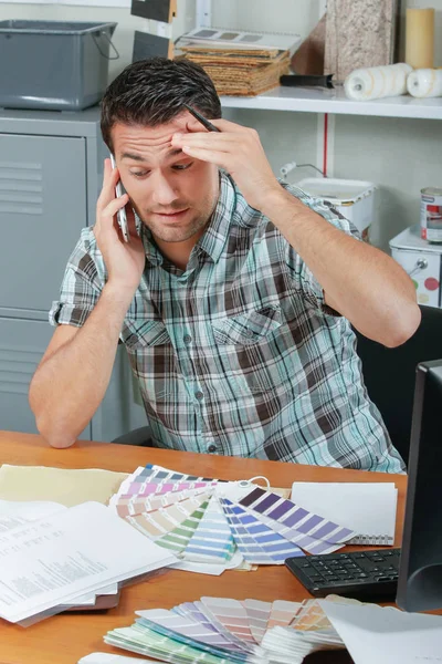 Ο άνθρωπος στο γραφείο με τα διαγράμματα χρώματος, και ξύνοντας το κεφάλι του — Φωτογραφία Αρχείου