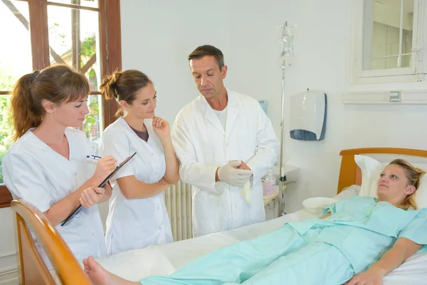 Three medical staff standing around patient s bed — Stock Photo, Image