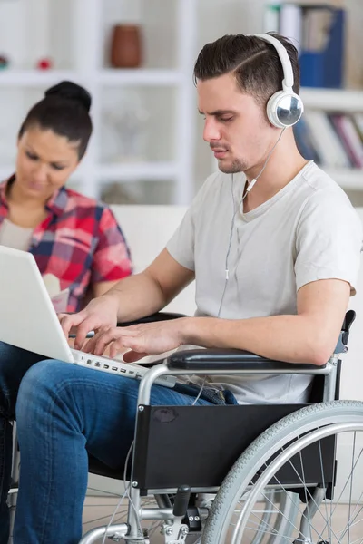 Człowiek z laptopa na wózku inwalidzkim z kobietą na bok — Zdjęcie stockowe
