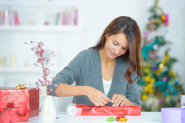 Beautiful young woman wrapping a gift in living room — Stock Photo, Image