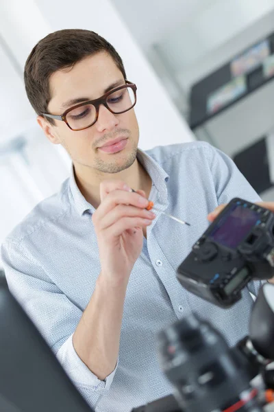 Jovem técnico confiante está consertando e limpando um cameralense digital — Fotografia de Stock