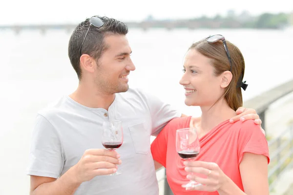 Casal abraçando, segurando copos de vinho ao lado do rio — Fotografia de Stock